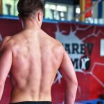 Shirtless man showcasing muscular back indoors in fitness gym.