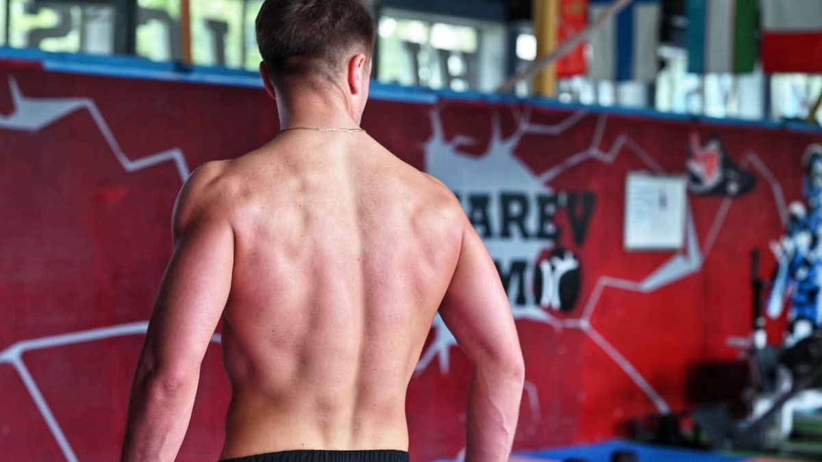 Shirtless man showcasing muscular back indoors in fitness gym.